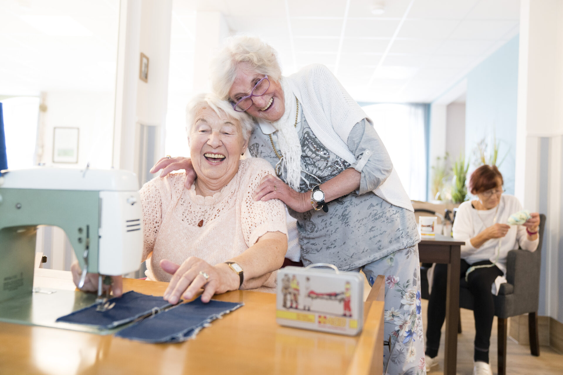 Zwei Seniorinnen machen gemeinsam Näharbeit und lachen.