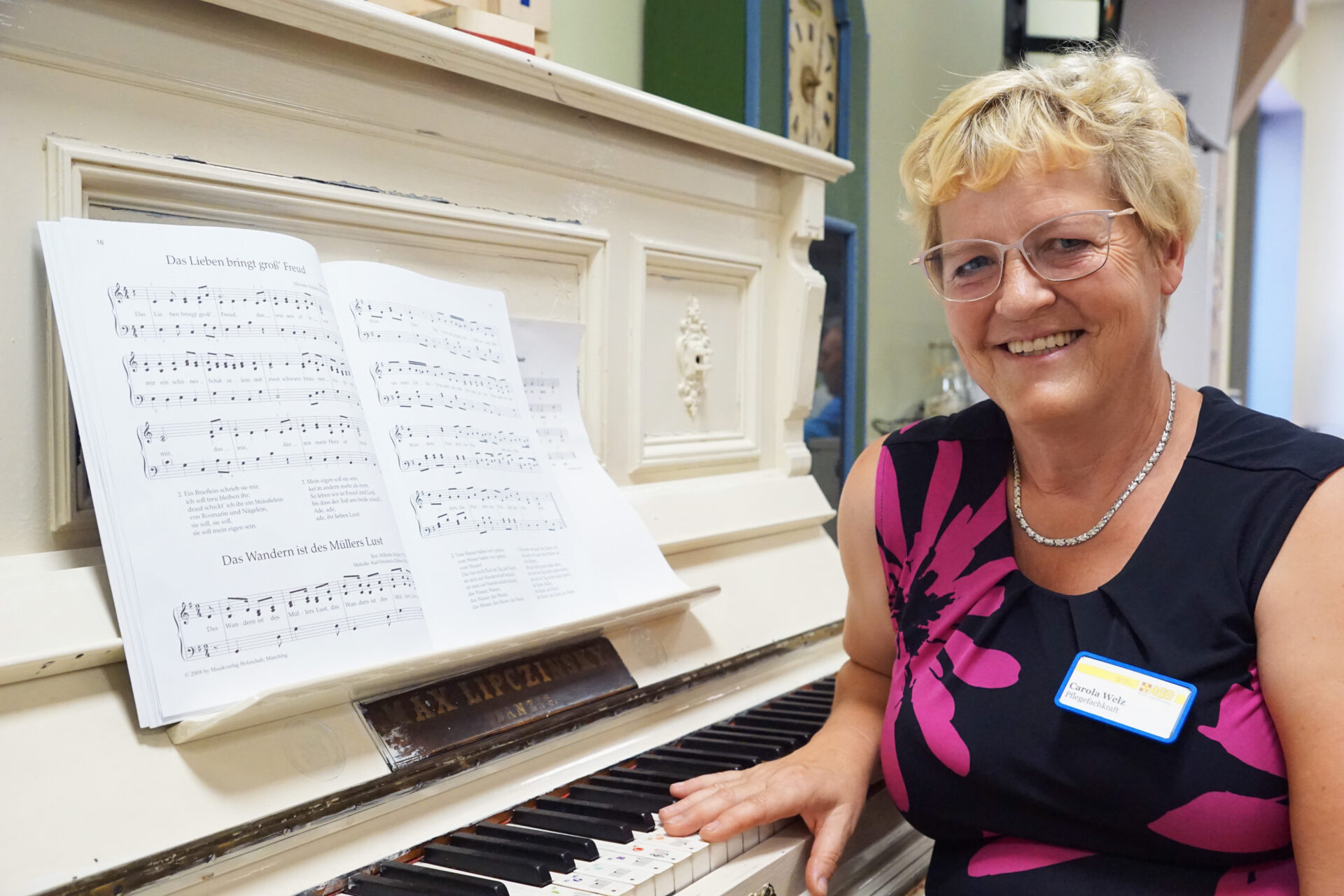 Eine Frau sitzt an einem Klavier und schaut lächelnd in die Kamera.