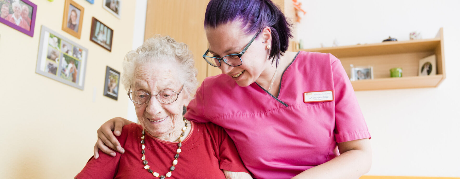 Eine Pflegekraft schaut sich gemeinsam mit einer Seniorin alte Familienfotos an.