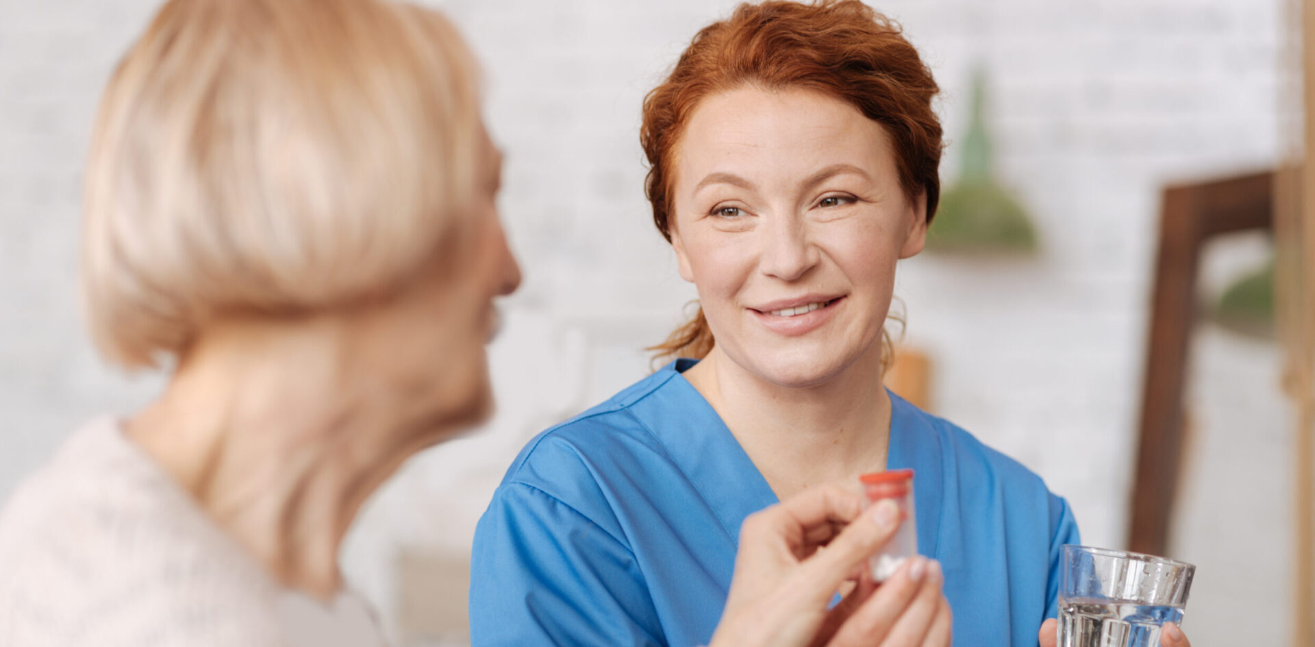 Eine Pflegeleiterin gibt einer Seniorin Tabletten.
