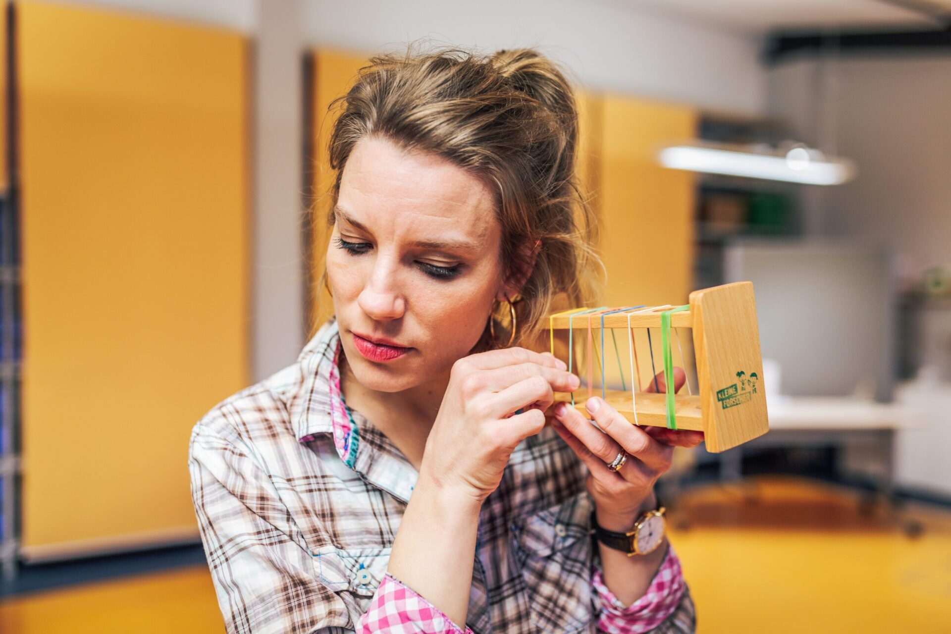 Eine Frau hält ein Instrument mit Gummibändern an ihr Ohr und zupft daran.