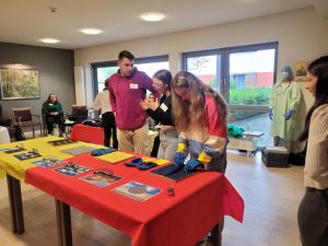3 junge Menschen stehen an einem Tisch und setzen sich Brillen auf, die Augenkrankheiten nachahmen sollen.