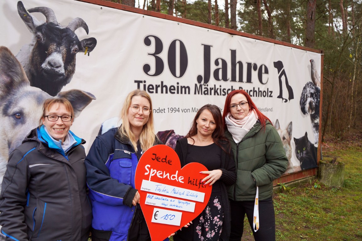 Vier Damen stehen vor einem großen Banner des Tierheims Märkisch Buchholz und schauen freundlich in die Kamera. Zwei von ihnen halten ein großes rotes Herz in der Hand, auf welchem ein Spendenbetrag steht.